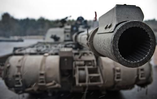 A close-up of a tank's main gun barrel, in focus, with the body of the tank out of focus in the background.