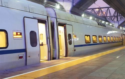 A train standing at a platform in the evening, lights on and doors open.